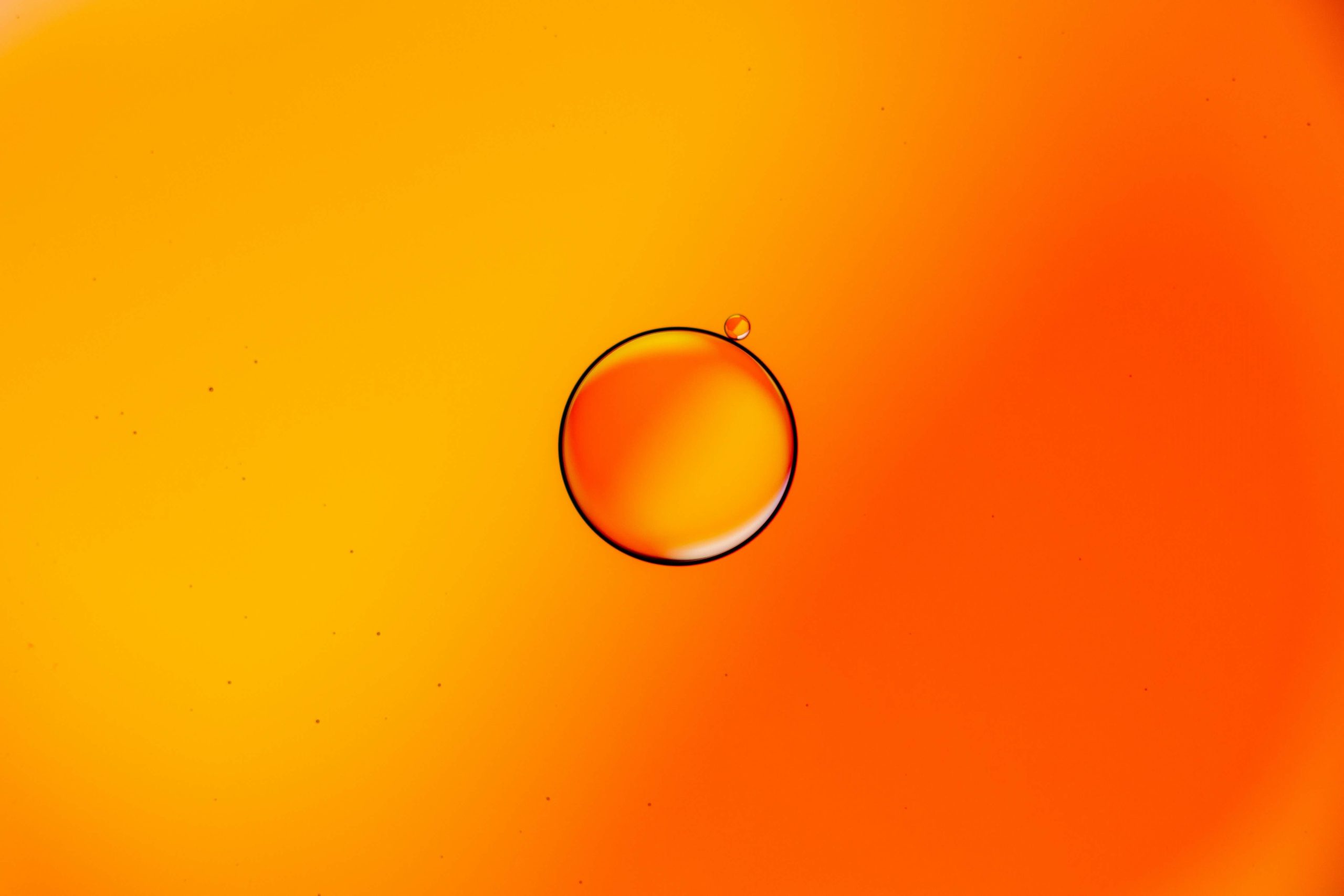 OilDropsOnWaterFleetwoodLancashireUKPeteGodfreyApril2021 Large and Little Drops of Oil Floating on Water Against Orange Background